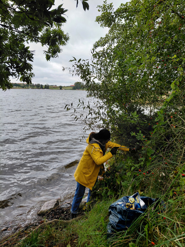 Wolontariusz sprzątający brzeg jeziora na Mazurach, zbieranie plastikowych butelek i odpadów.