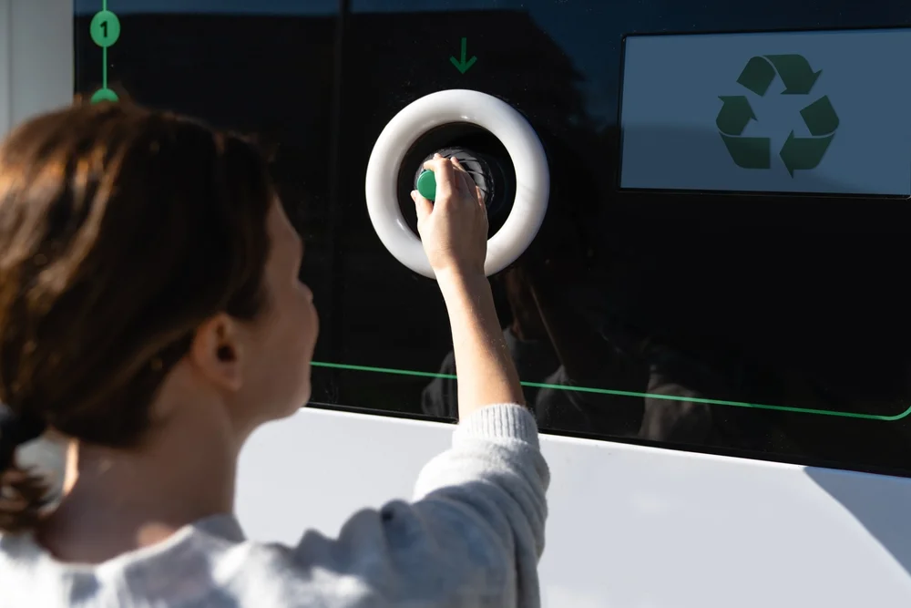 Kobieta wrzuca plastikową butelkę do automatu kaucyjnego – system kaucyjny w Polsce od 1 października 2025 roku